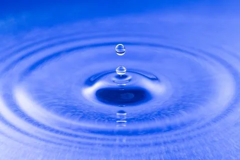 Close-up of a water drop falling into blue liquid creating ripples Fotos Stock
