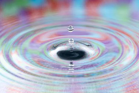 Close-up of a water drop falling into colorful rippling liquid surface Fotos Stock