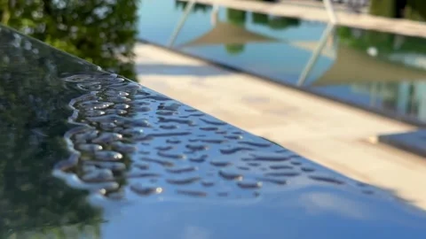 Close-up of water droplets on pool edge with blurred garden background Stock Footage 282532350
