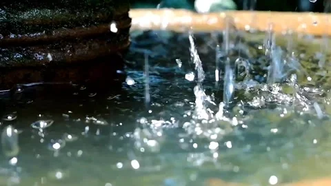 Close-up of water droplets splashing into a rustic stone fountain bowl Stock Footage 315530286