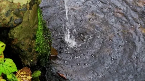 Close up of water drops falling on dark wet rock surface forming ripples and Stock Footage 329212879