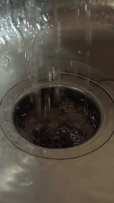 Close up of water flowing into metallic kitchen sink drain with splashes and Video stock 344415599