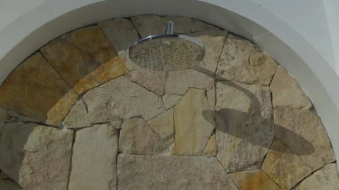 Close-up of water flowing from a shower head mounted on a natural stone wall Stock Footage 339197506