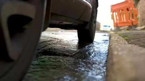 Close up of water flowing underneath car. holes apearing in road tarmac causing Stock Footage 145611149