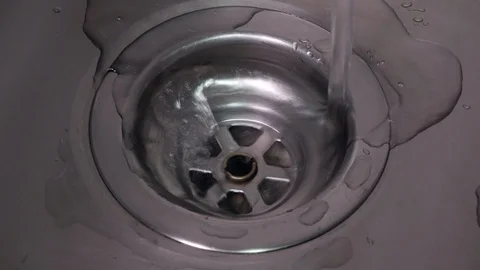 Close up of water running down plug hole in a modern stainless steel sink Stock Footage 104782976