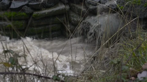 Close up of water surging out of a pipe into a roadside drainage ditch Stock Footage 68950647