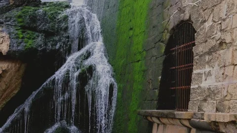 Close up waterfall flows beside a medieval wall with a barred door. Video stock 263920843