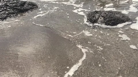 Close up of wave flowing over rock on sand beach Stock Footage 272578425