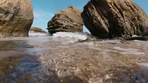 A close-up wave rolls over the camera on the shore of a sandy beach against the Vídeos de archivo 150680455