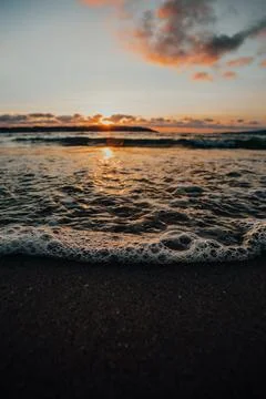 Close   up   of   waves   and   bubbles   on   the   shore   at   sunset Stock Photos