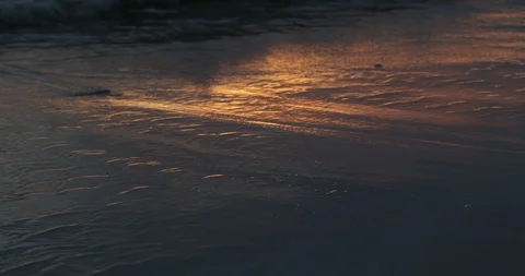 Close up of waves breaking at sandy shore at golden hour. Orange reflection 스톡 동영상 119062419