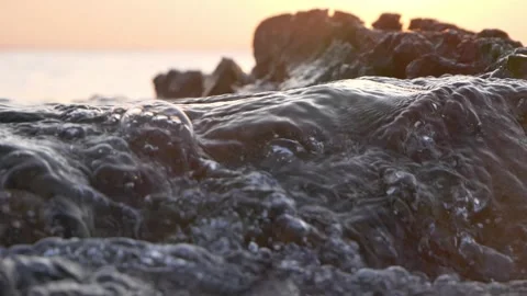 Close-Up Waves Crashing Over Rocky Shoreline at Sunset Stock Footage 337404639