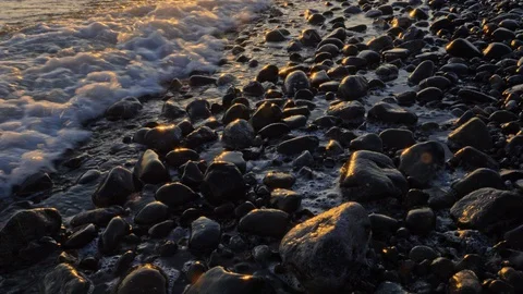 Close up of waves rolling over rocks with reflection of sunrise in slow motion Stock Footage 128623737