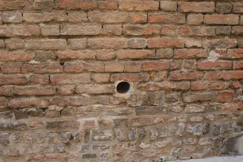 Close up weathered aged red brick wall texture with a circular hole showing Stock Photos