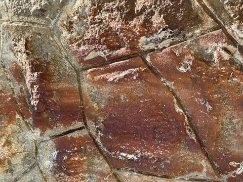 Close-up of a weathered red stone surface with cracks, rust stains, and tex.. Foto stock