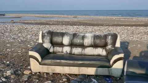 Close-up of a weathered sofa left on a rocky beach by the sea Stock Footage 317966859