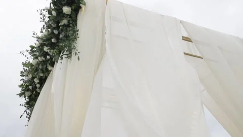A close-up of a wedding arch decorated with white flowers, greenery, and draped Stock Footage 322558613