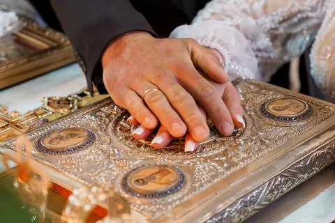 Close-up of wedding couple placing hands on ornate golden religious book du.. Stock Photos