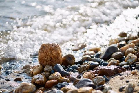 Close-up of wet pebbles on a sunny beach with gentle sea waves washing ashore 库存照片