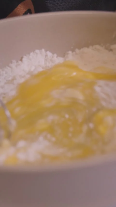 Close-up of whisk mixing flour, egg and water into batter in a mixing bowl in a Stock Footage 329265386