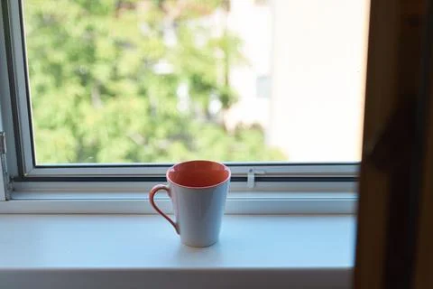 Close-up of a white and pink ceramic coffee mug sitting on a windowsill 스톡 사진