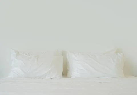 Close-up white bedding sheets and pillow on light wall room background. Stock Photos