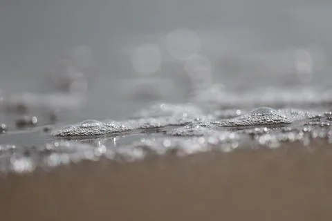 Close up of white bubbles on water surface from beach with blur sandy backgro Stock Photos