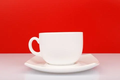 Close up of white ceramic coffee or tea cup on white table against red Stock Photos