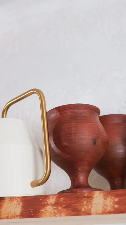 Close up of white ceramic pitcher with golden handle and wooden goblets on Vidéo 344414850