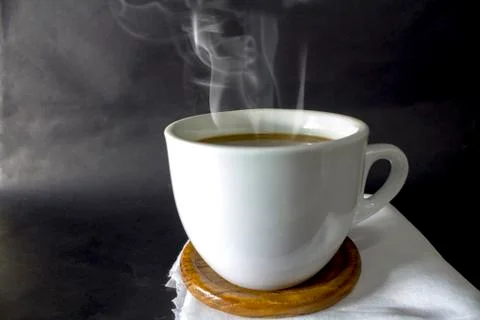 Close up of a white coffee cup with hot smoke resting on a white cloth on a b Stock Photos