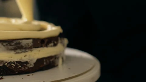 Close up of white cream is being put to the chocolate cake by confectioner. Stock Footage 89959106