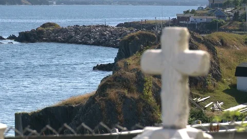 Close up of white cross in focus with hills and sea, Newfoundland, Canada Stock Footage 132396867