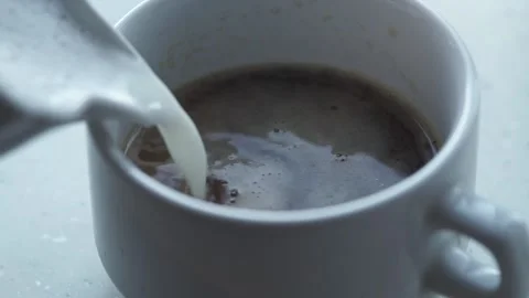 A close-up of a white cup of coffee into which milk and foam are poured. Stock Footage 201291751