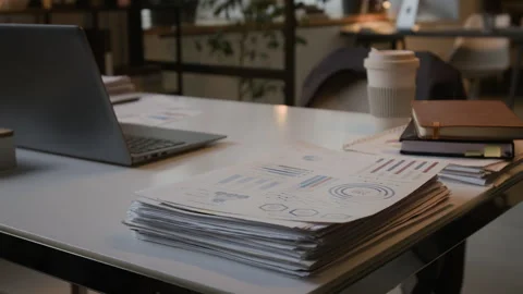 Close-up of White Desk with Open Laptop, and Stack of Documents with Graphs Stock Footage 330479406