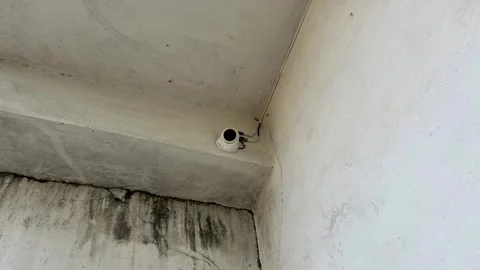 Close up of a white dome security camera installed on a concrete building wall Видео 328409119