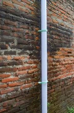 A close up of a white downspout pipe secured with green clips against an ol.. Stock Photos