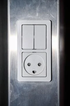 Close-up of a white electrical outlet and a switch on a metal wall. Stock Photos