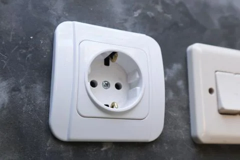 Close-up of a white electrical power socket next to a light switch on a raw.. Stock Photos