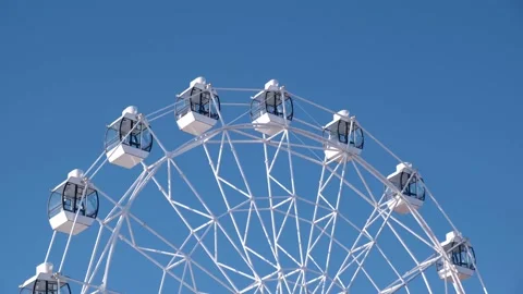 Close-up of white Ferris wheel slowly rotating against the blue sky on sunny day Stock Footage 172563586