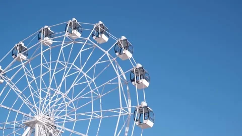 Close-up of white Ferris wheel slowly rotating against the blue sky on sunny day Stock Footage 175019915