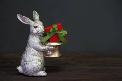 Close-up of a white-golden statuette of an Easter bunny holding a red gift bo Stock Photos