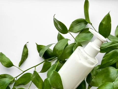 Close up of white lotion bottle surrounded by green leaves on white background Stock Photos