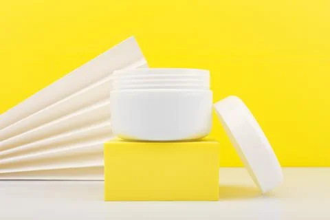 Close up of white opened jar on white table against yellow background decorated Stock Photos