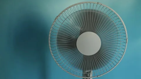 Close-up of a white oscillating fan blades spinning against a blue background Stock Footage 340266297