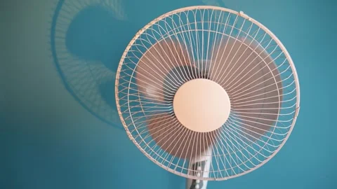 Close-up of a white oscillating fan blades spinning against a blue wall Stock Footage 340266622