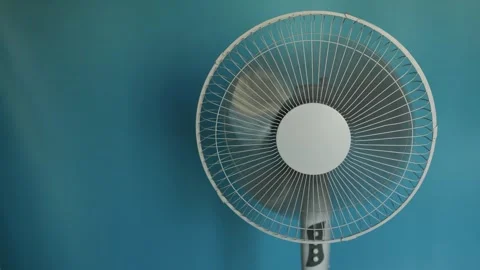 Close-up of a white oscillating fan spinning on a blue background Stock Footage 340266393