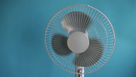 Close-up of a white oscillating fan spinning against a blue background Stock Footage 340266486
