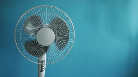 Close-up of a white oscillating fan spinning on a blue background Stock Footage 340267448