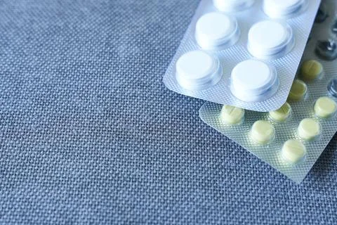 Close up of white pills in blister pack on blue fabric background. Stock Photos