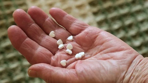 Close-up of white pills in the shape of hearts pouring into the hand of an Stock Footage 268590307
